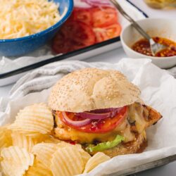 Juicy cheeseburger with fresh vegetables and potato chips on baking tray.