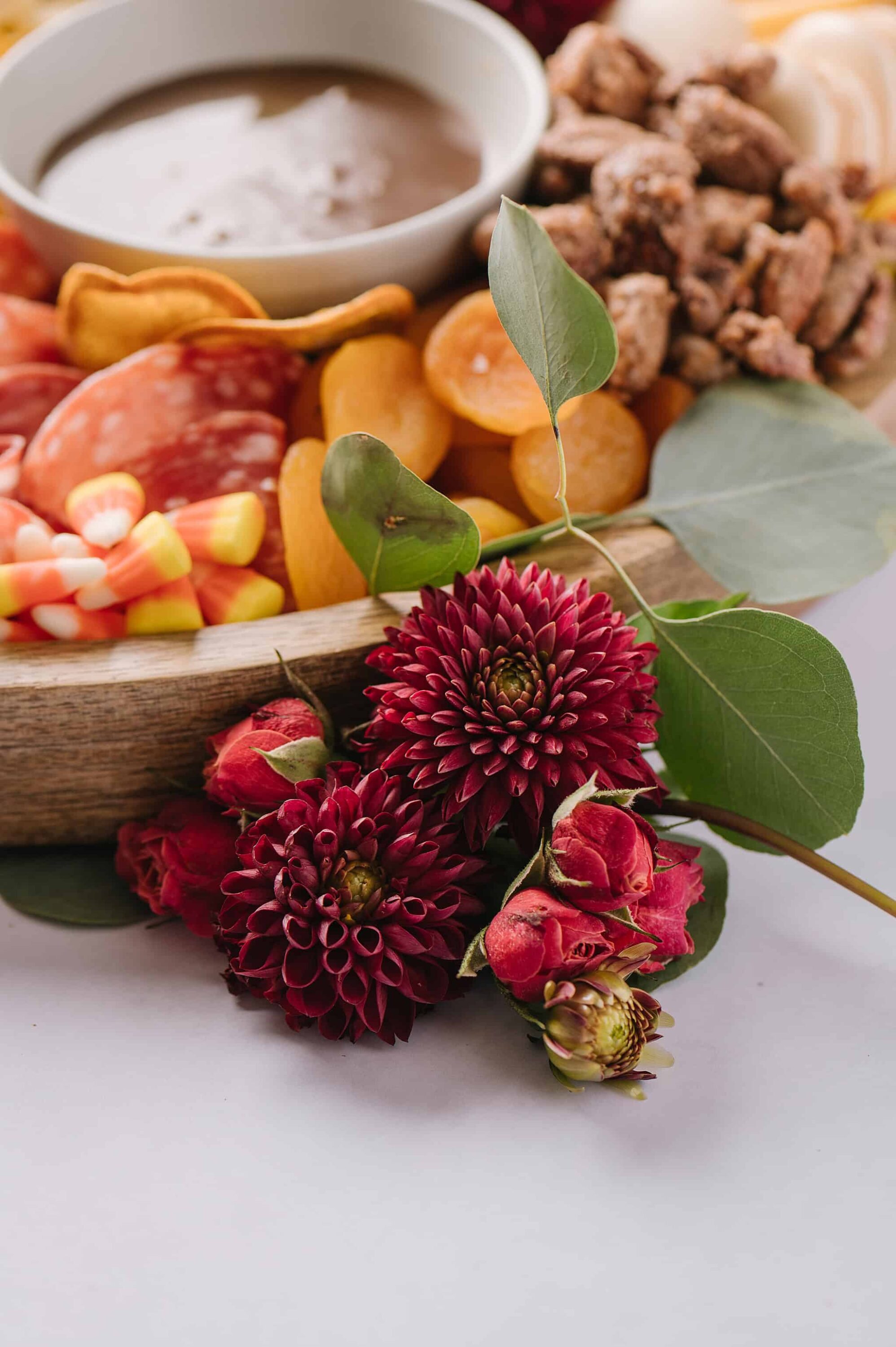 Delicious party platter with assorted meats, cheeses, candies, and dips on a wooden tray.