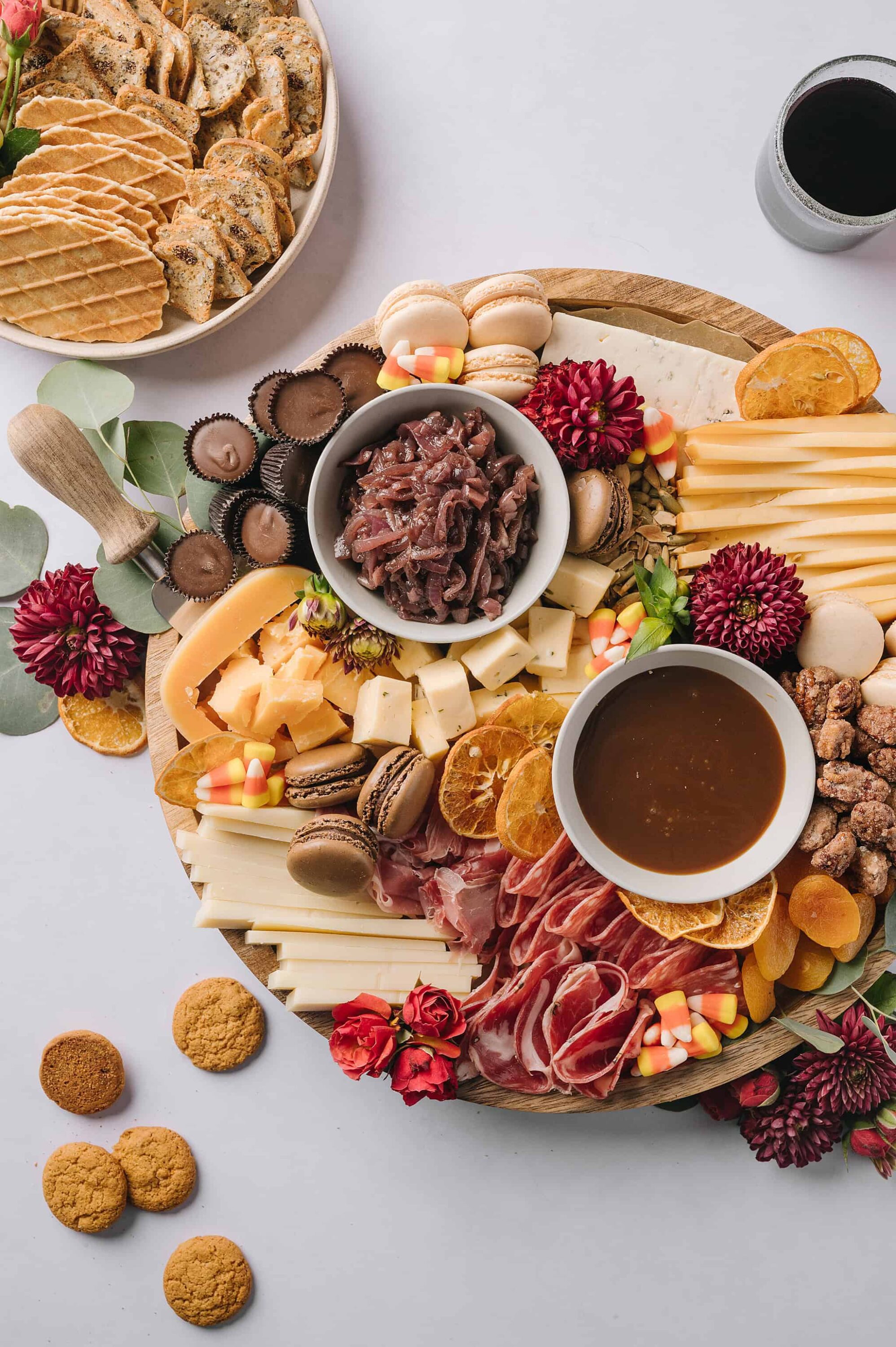 Cheese and charcuterie board with dried fruits, candies, and desserts on a wooden platter.