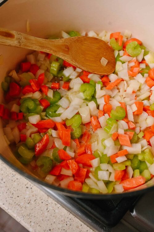 Diced vegetables sizzling in a pot for soup or stew, with a wooden spoon for stirring.