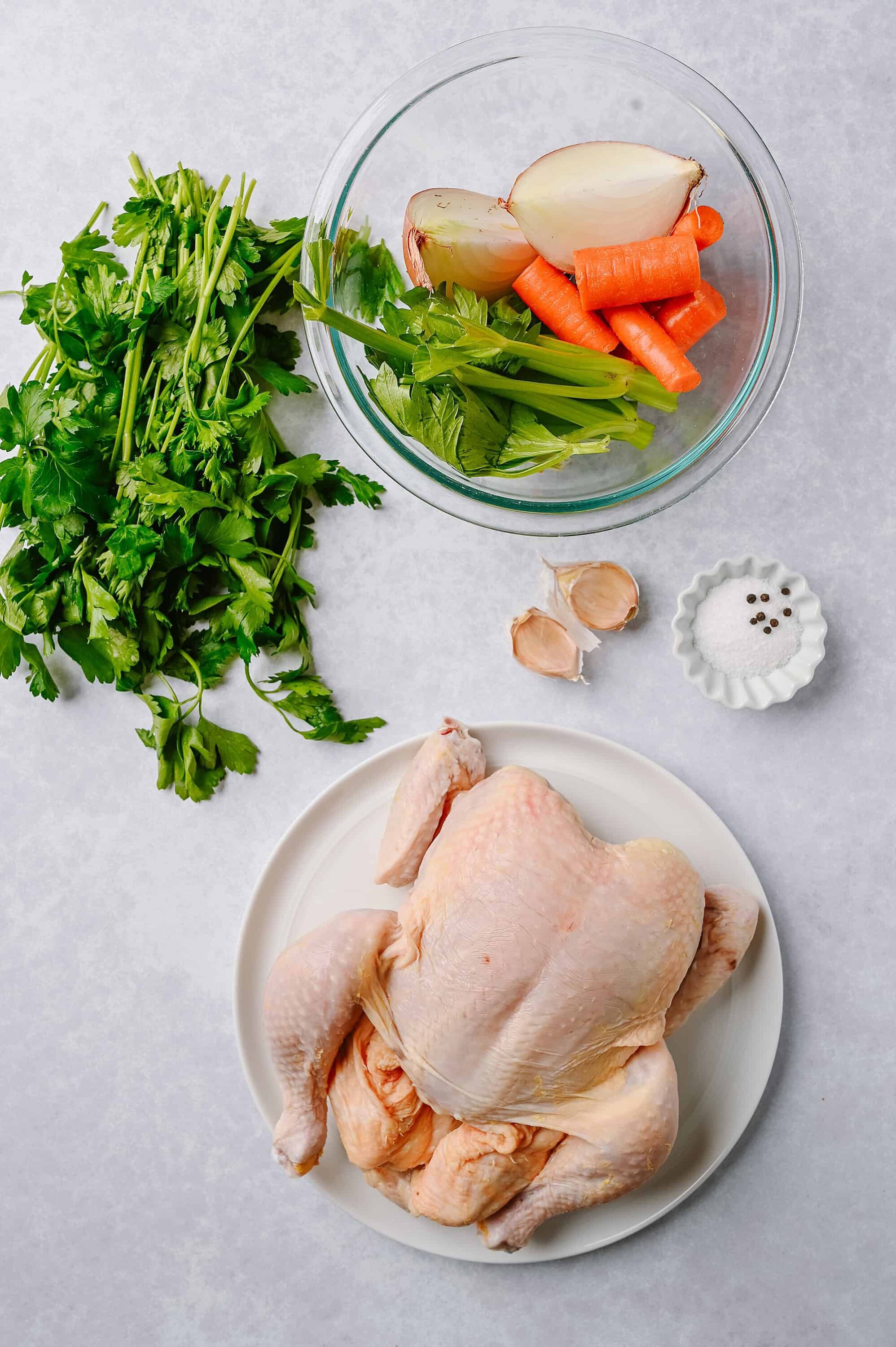 Fresh whole chicken with vegetables for roasting or cooking recipes. Includes carrots, onions, garlic, celery, and herbs.