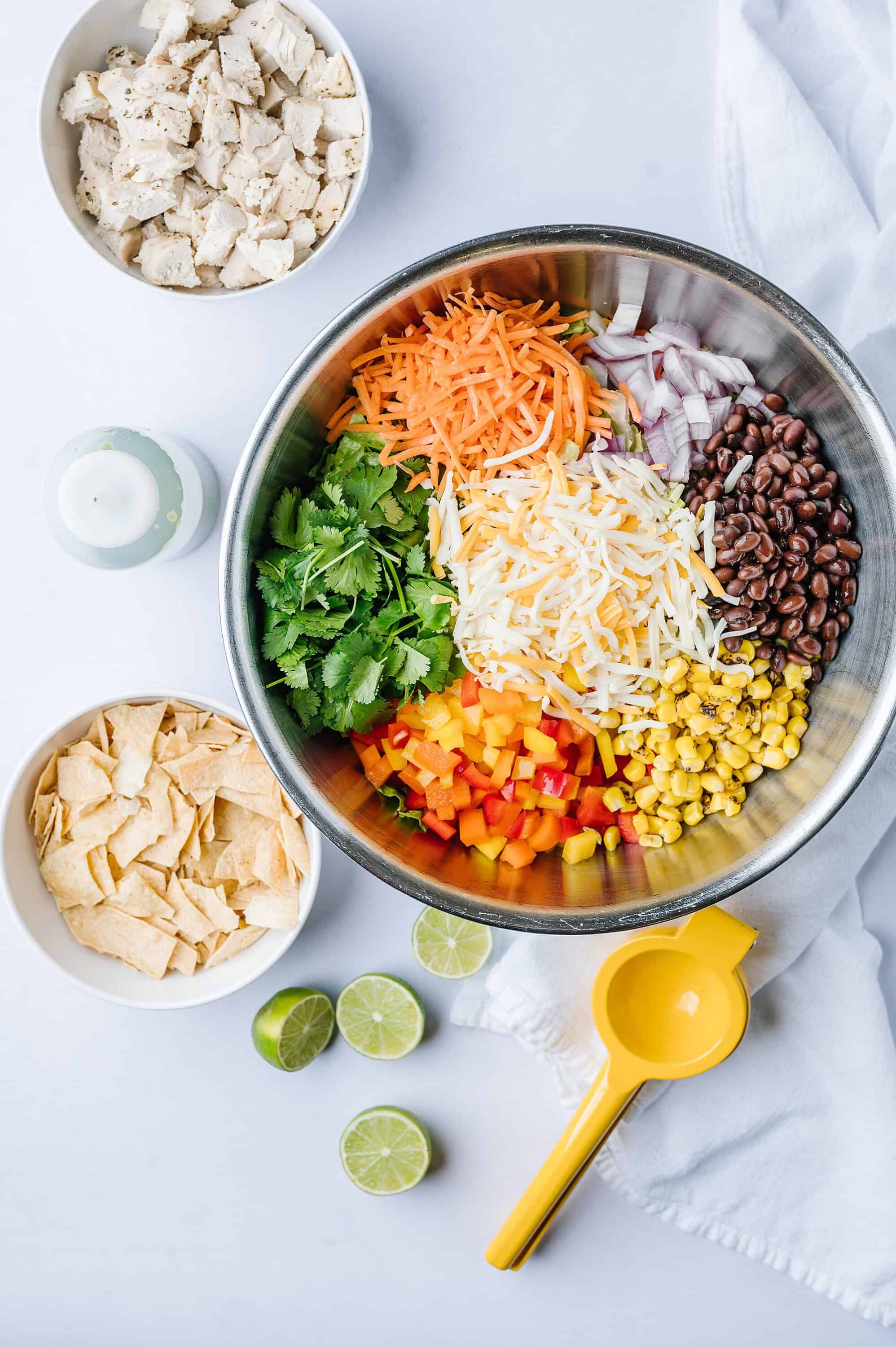 Chopped cooked chicken, shredded cheese, black beans, corn, and vegetables in a mixing bowl for taco salad.
