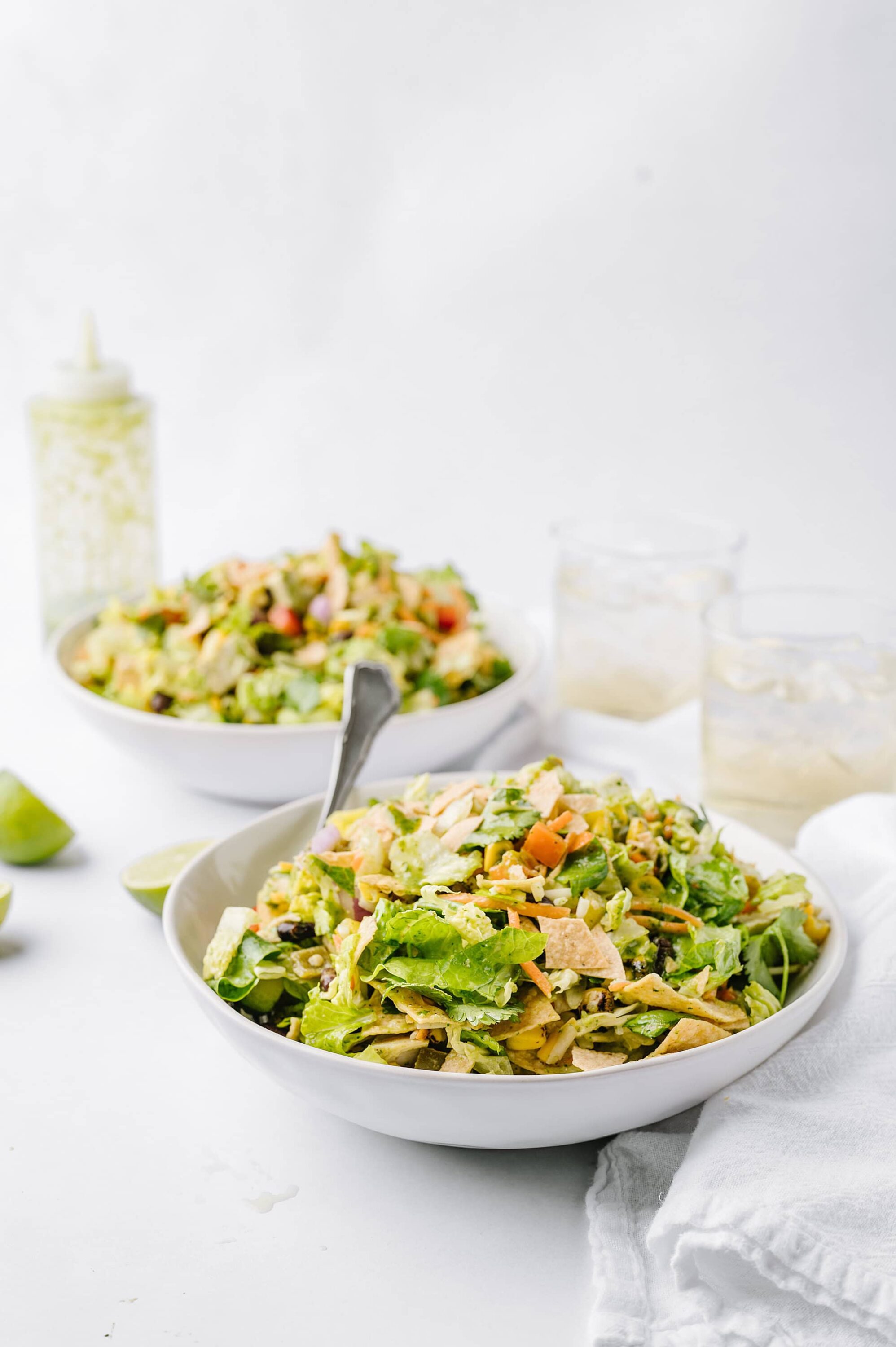 Fresh homemade chicken Caesar salad in white bowls with lime wedges and dressing on a white background.