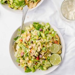 Fresh veggie chicken Caesar salad with lime wedges on white background.