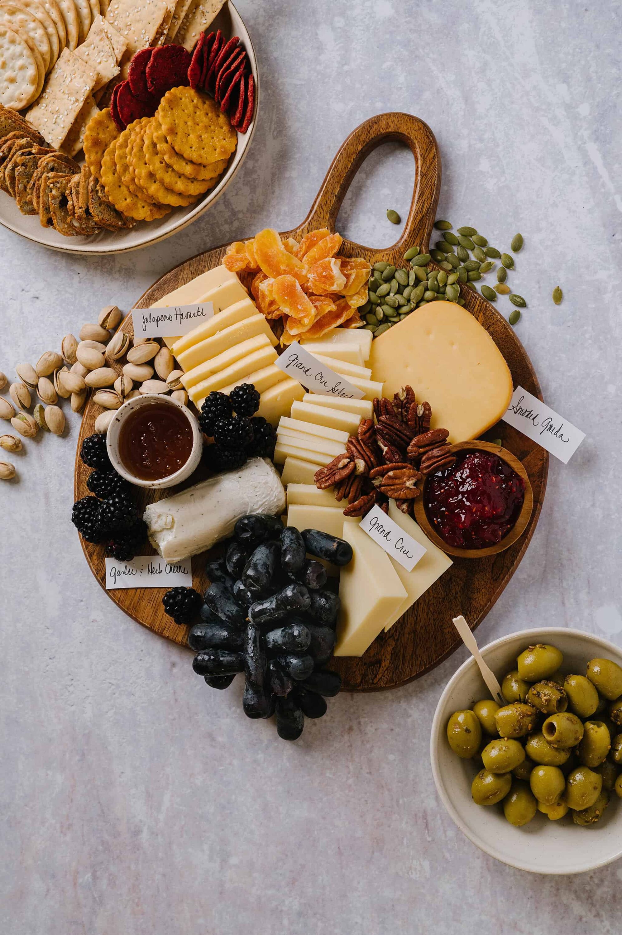 Assorted cheese and fruit platter with nuts, seeds, and jam for a cheese board or wine pairing event.