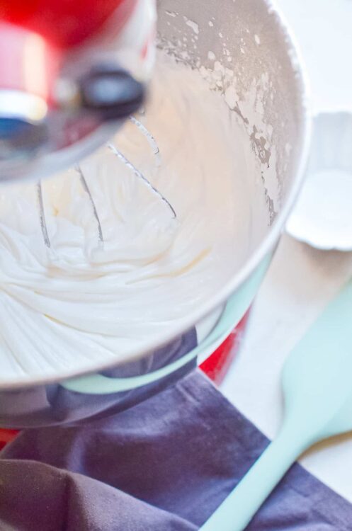 Cream being mixed in a stand mixer with a beater attachment.