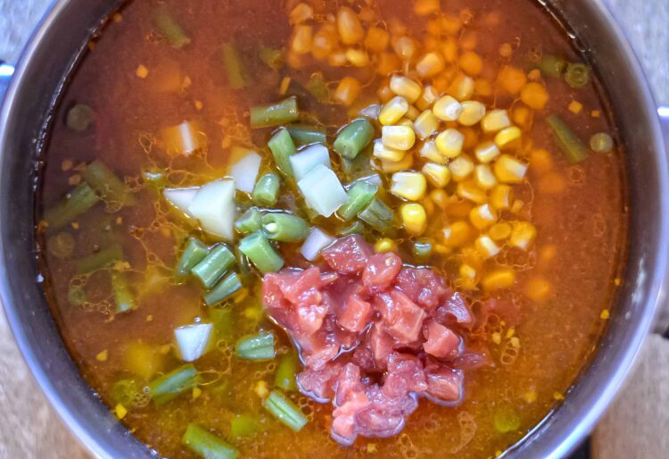 Savory soup with diced tomatoes, corn, and chopped green onions in a pot.
