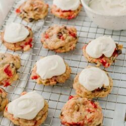 Cream cheese strawberry scones on cooling rack with whipped cream topping.