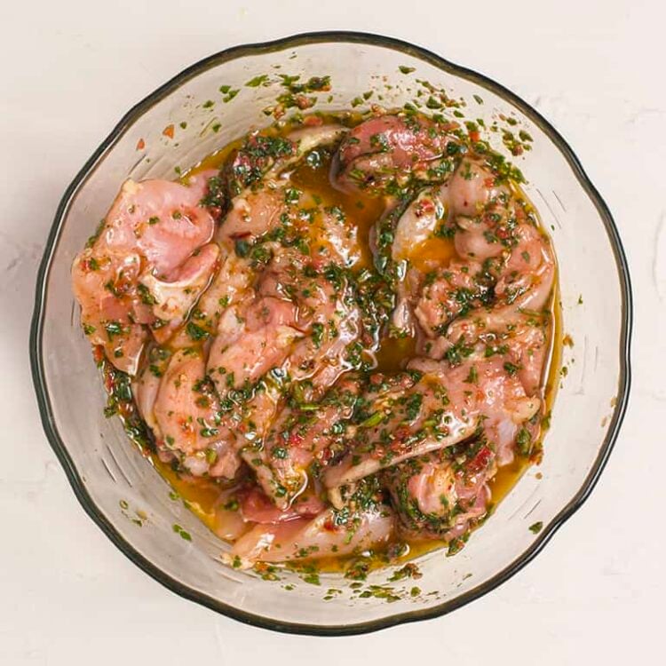 Marinated chicken thighs in herb and citrus marinade in a glass bowl for Baked Bree recipe.