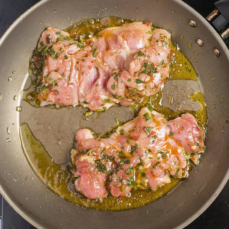 Juicy chicken thighs cooking in a skillet with herbs and oil.