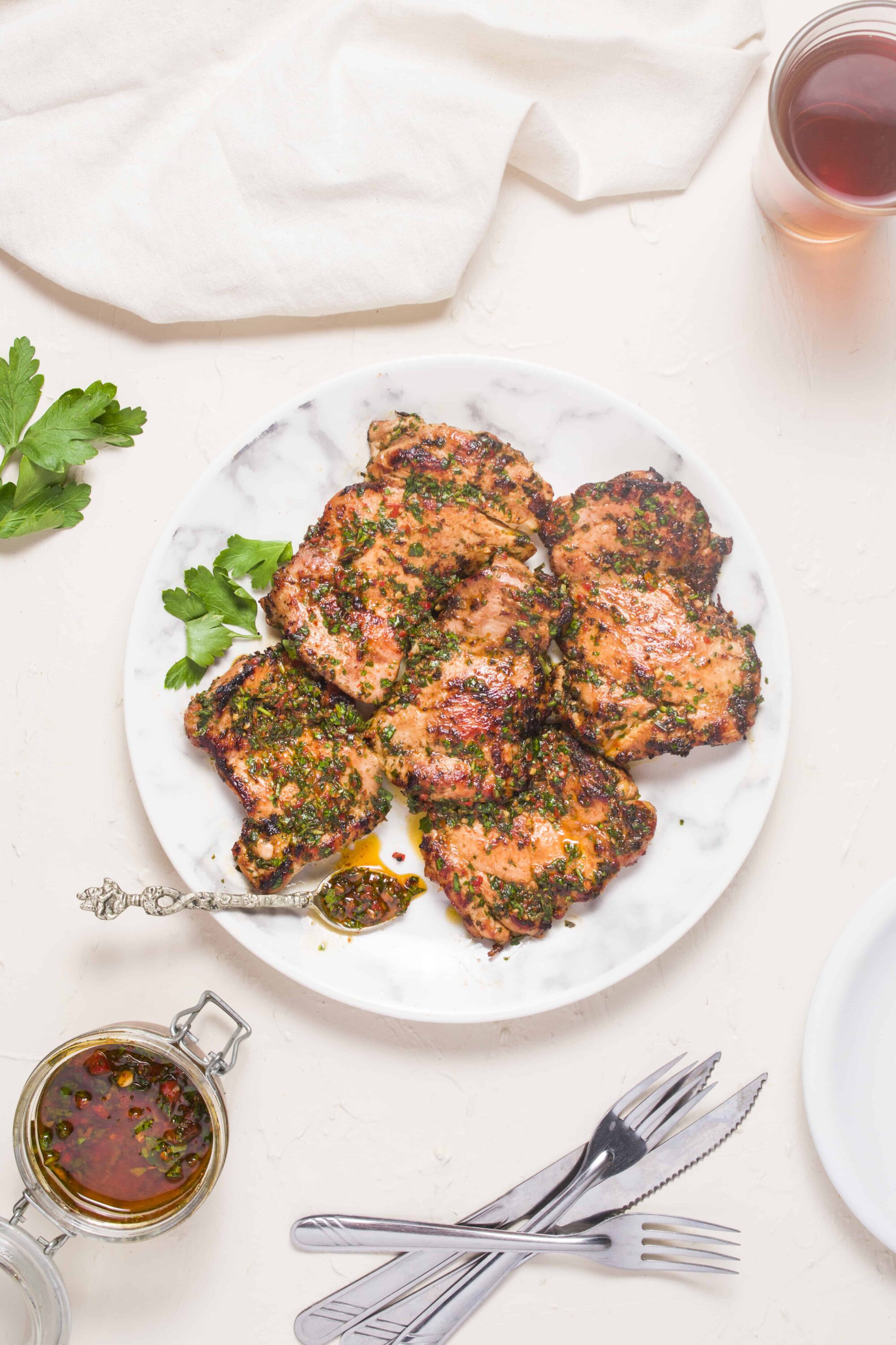 Succulent grilled chicken thighs with herbal marinade on white marble plate.