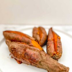 Roasted sweet potatoes with a smoky, caramelized skin and vibrant orange flesh on a white plate.