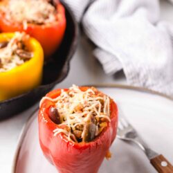 Fresh stuffed bell peppers with cheese, mushrooms, and rice on a white plate.
