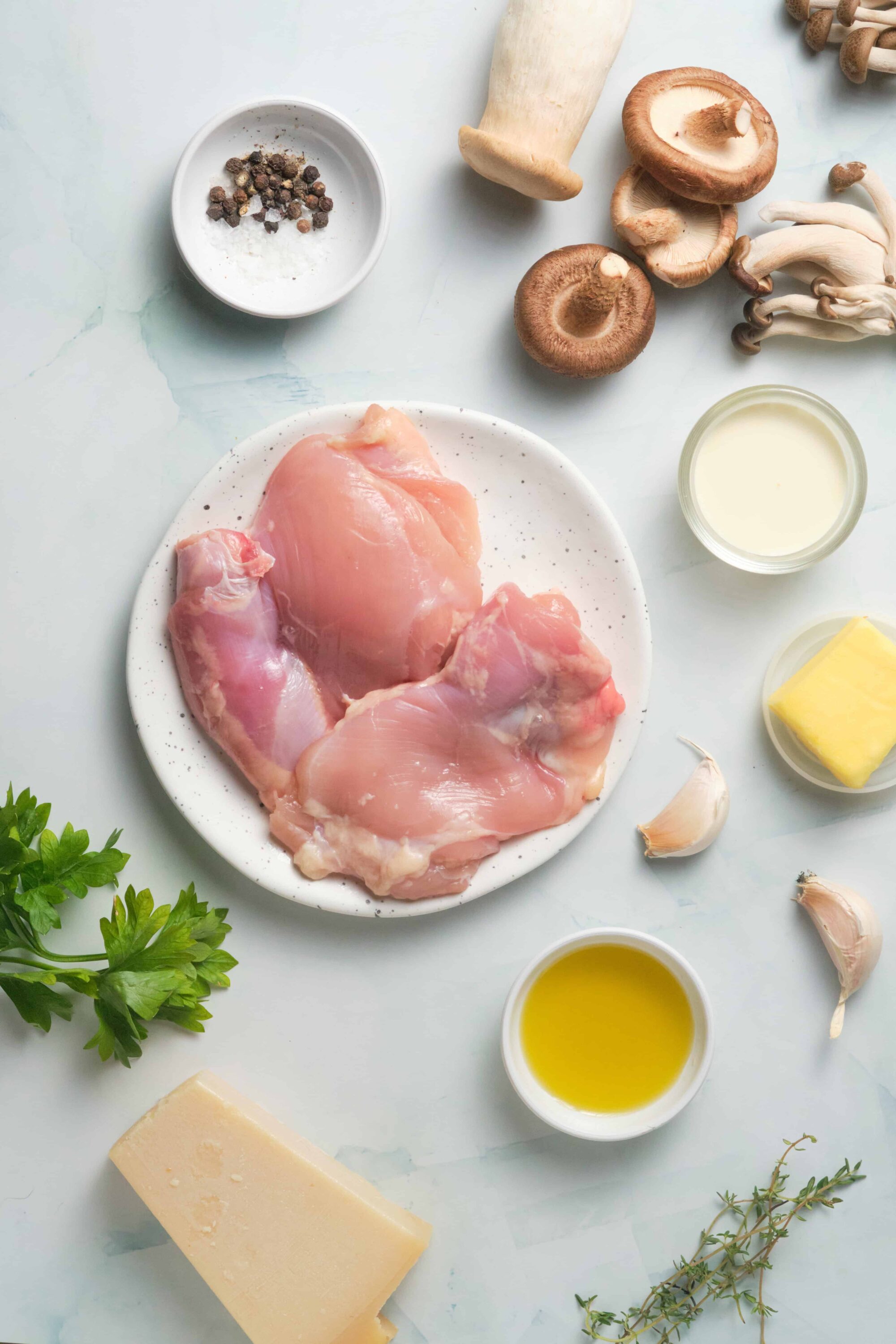Fresh raw chicken breast and thighs with garlic, mushrooms, herbs, and dairy ingredients for cooking or baking recipes.