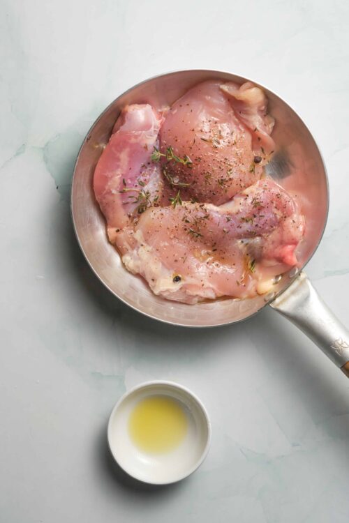 Boneless chicken thighs seasoned with herbs in a skillet, ready for cooking.