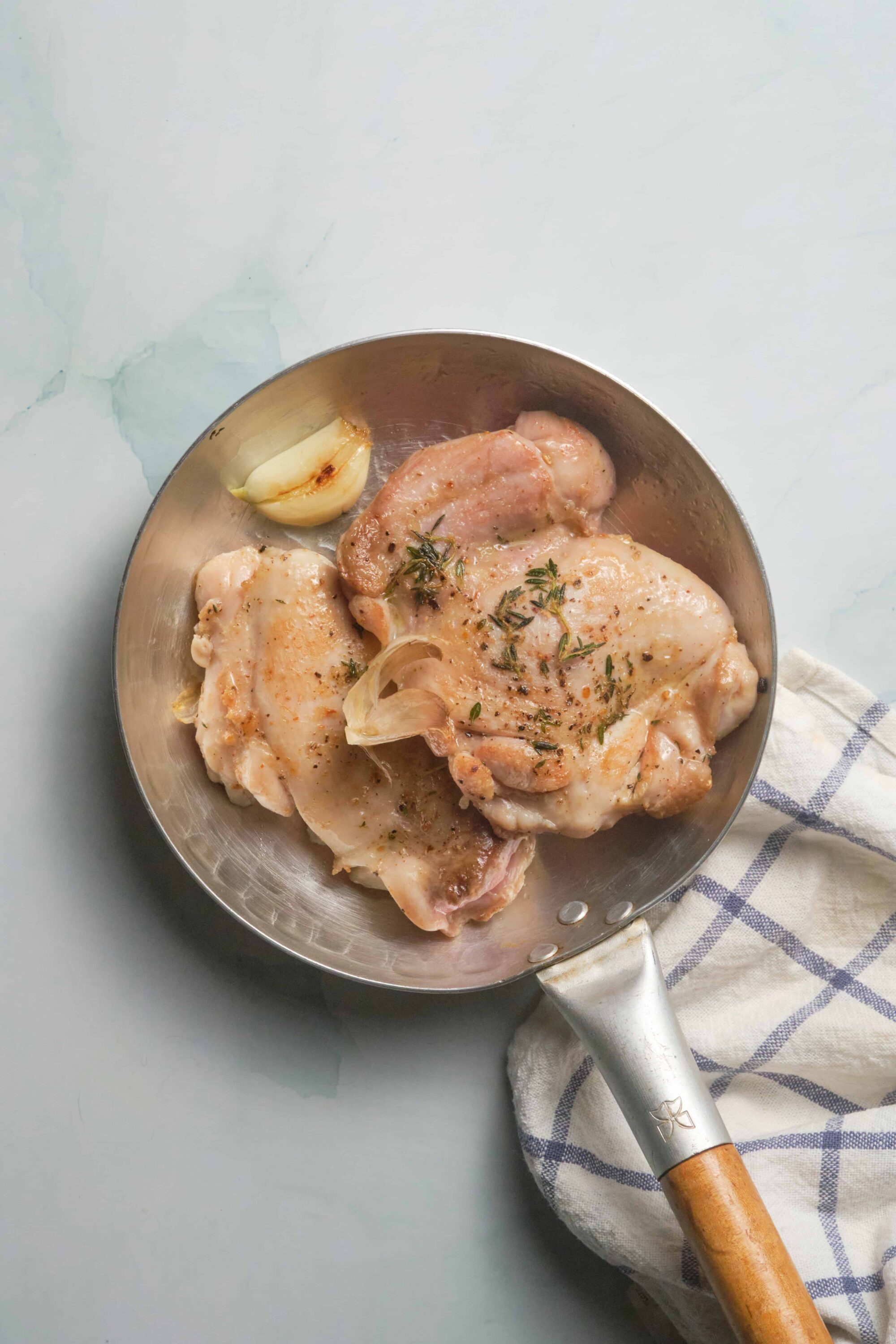 Juicy raw chicken thighs in a skillet with garlic and herbs ready for cooking.