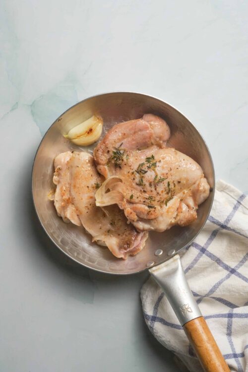 Juicy raw chicken thighs in a skillet with garlic and herbs ready for cooking.