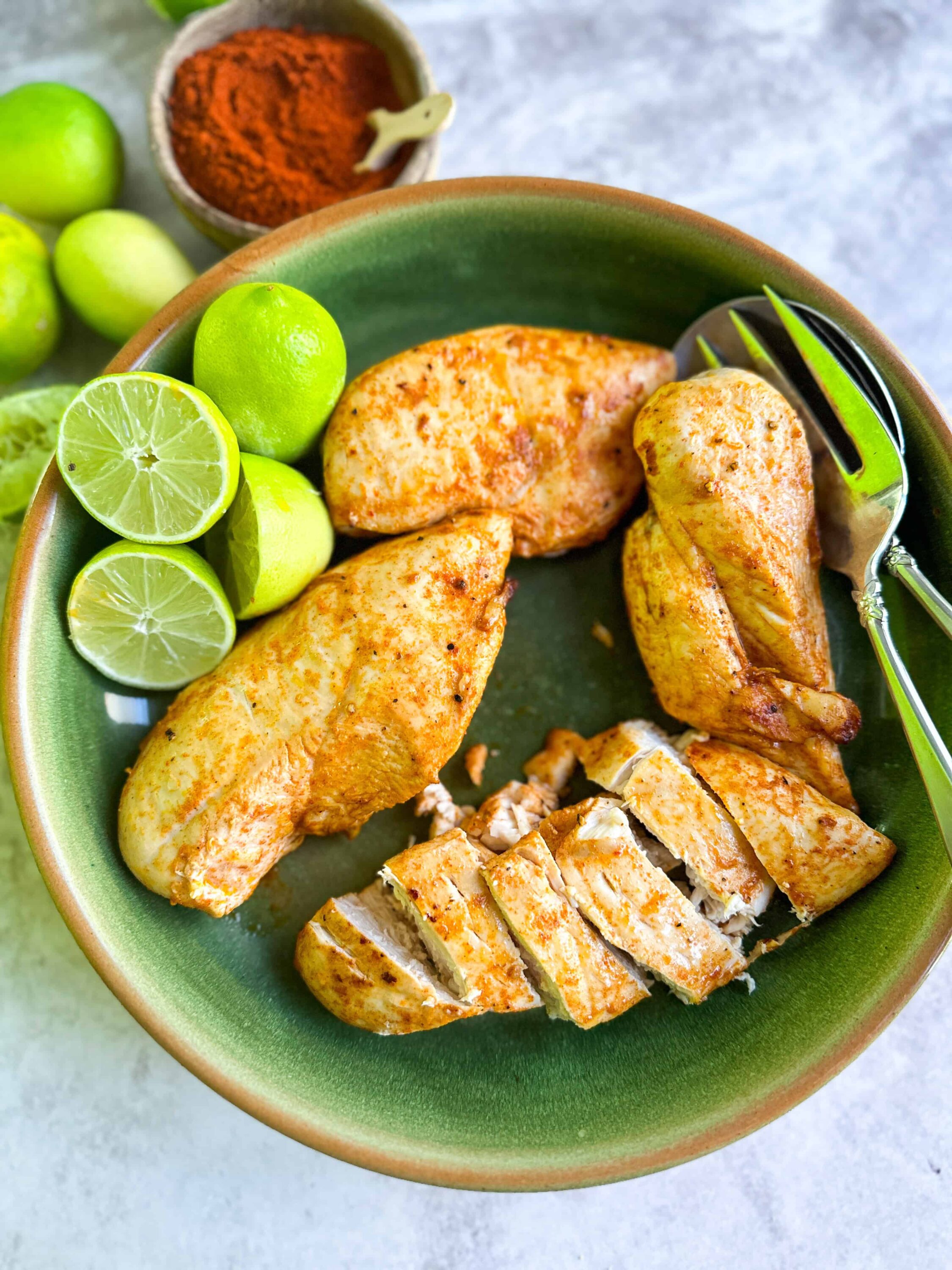 Juicy grilled chicken breast with lime wedges and fresh limes in a green bowl.