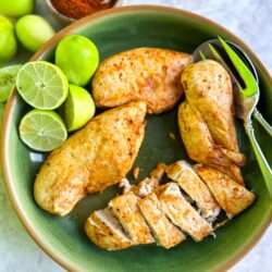 Juicy grilled chicken breast with lime wedges and fresh limes in a green bowl.