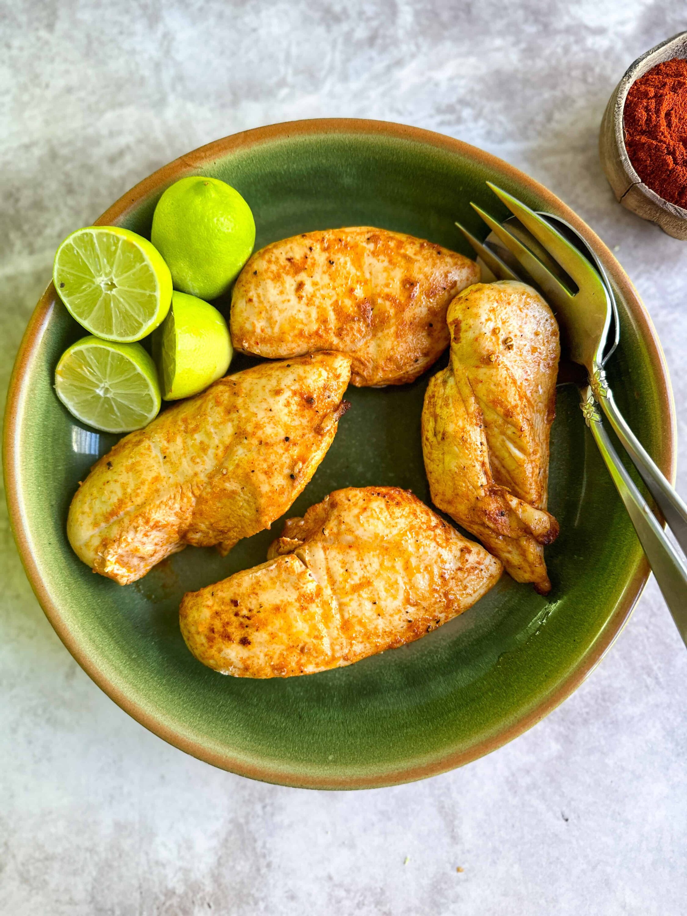 Grilled chicken breast with lime wedges on green ceramic plate for healthy eating.