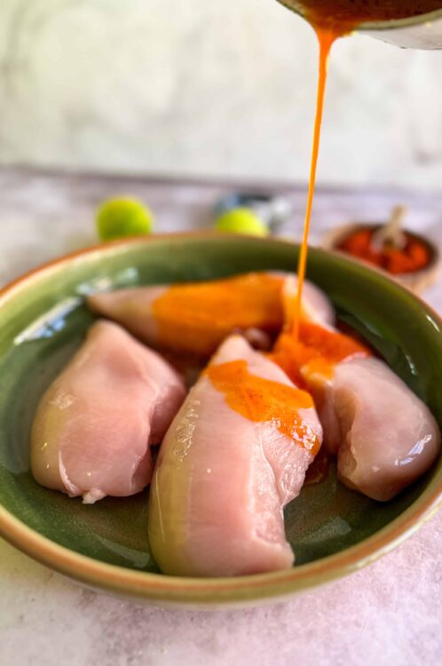 Succulent raw chicken breasts topped with spicy hot sauce in a green bowl.