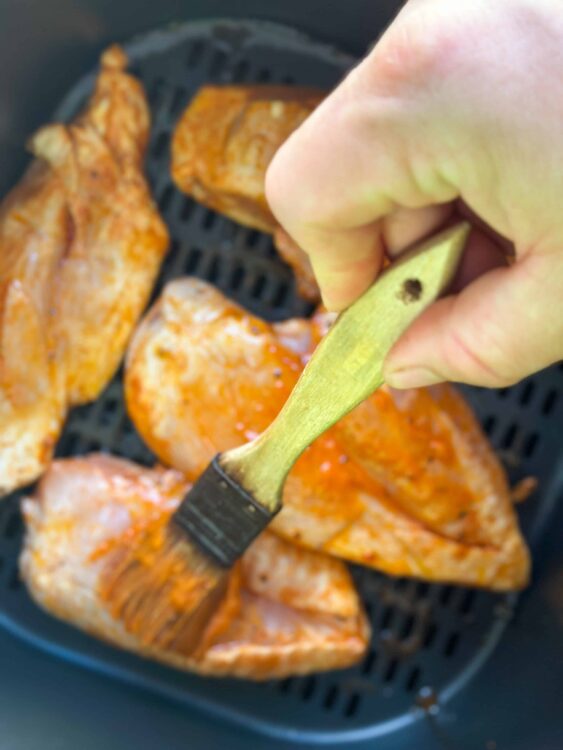 Golden-brown chicken pieces being brushed with marinade or sauce in an air fryer basket.