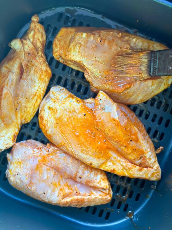 Juicy seasoned chicken breasts in an air fryer basket, ready for baking or serving.