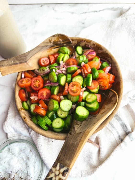 Fresh cucumber, cherry tomato, and red onion salad in a wooden bowl.