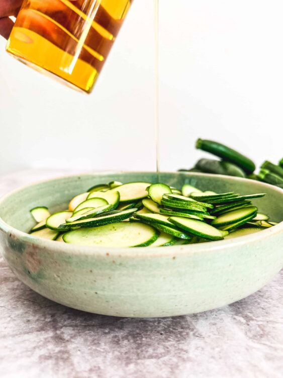 Sliced cucumbers in a green ceramic bowl with dressing being poured over.