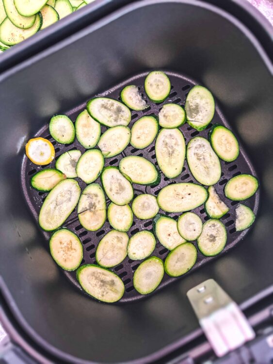 Sliced zucchini in an air fryer basket, ready for cooking.