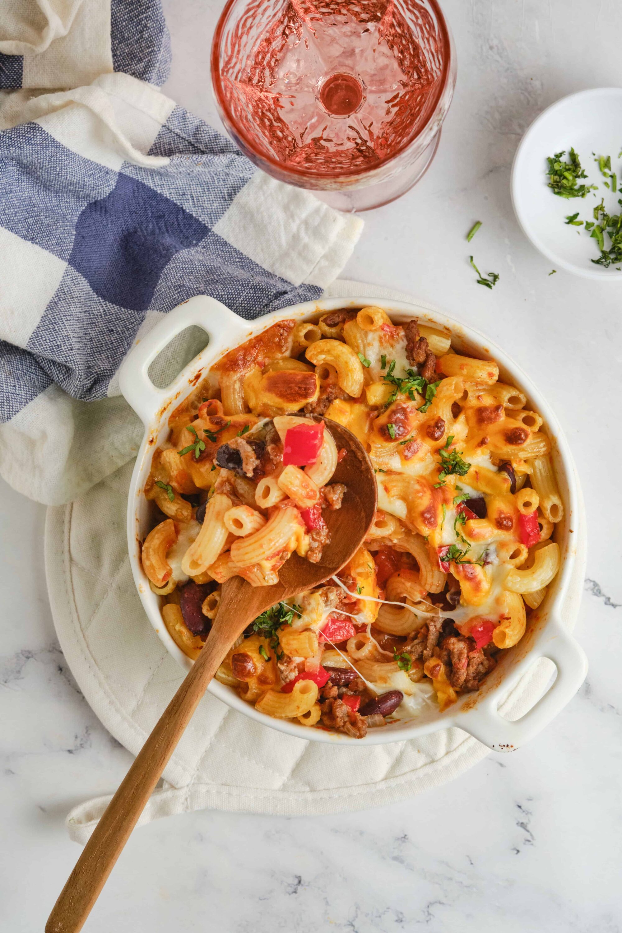 Baked pasta casserole with cheese, ground beef, and vegetables in a white baking dish.