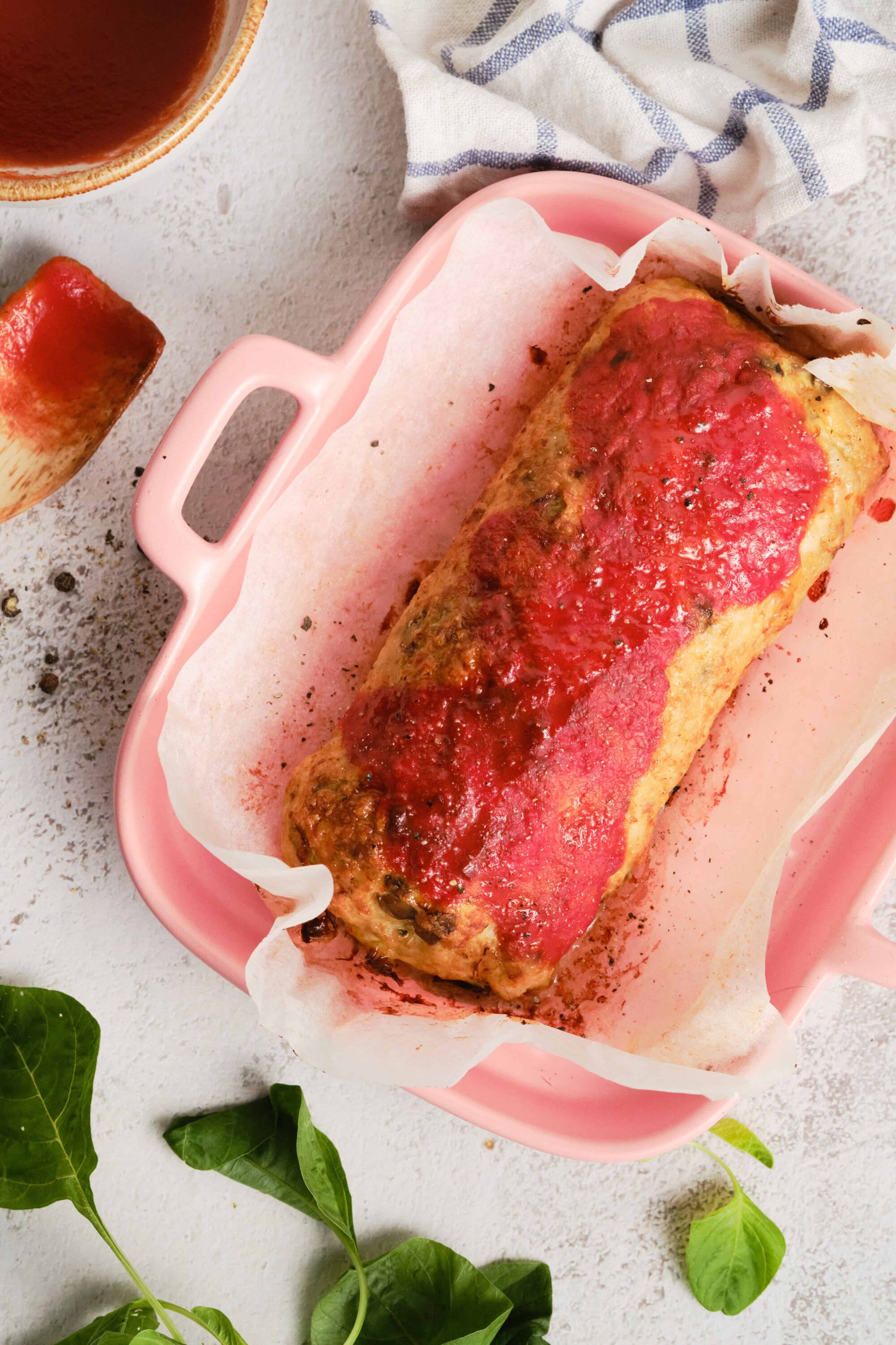 Juicy meatloaf with tomato glaze in pink baking dish on white surface.