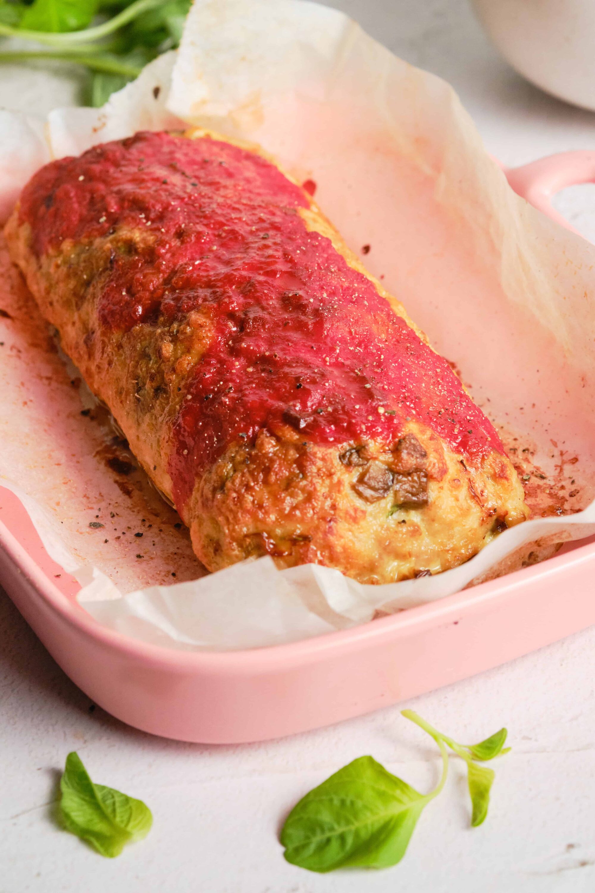 Baked meatloaf with tomato glaze in pink dish.