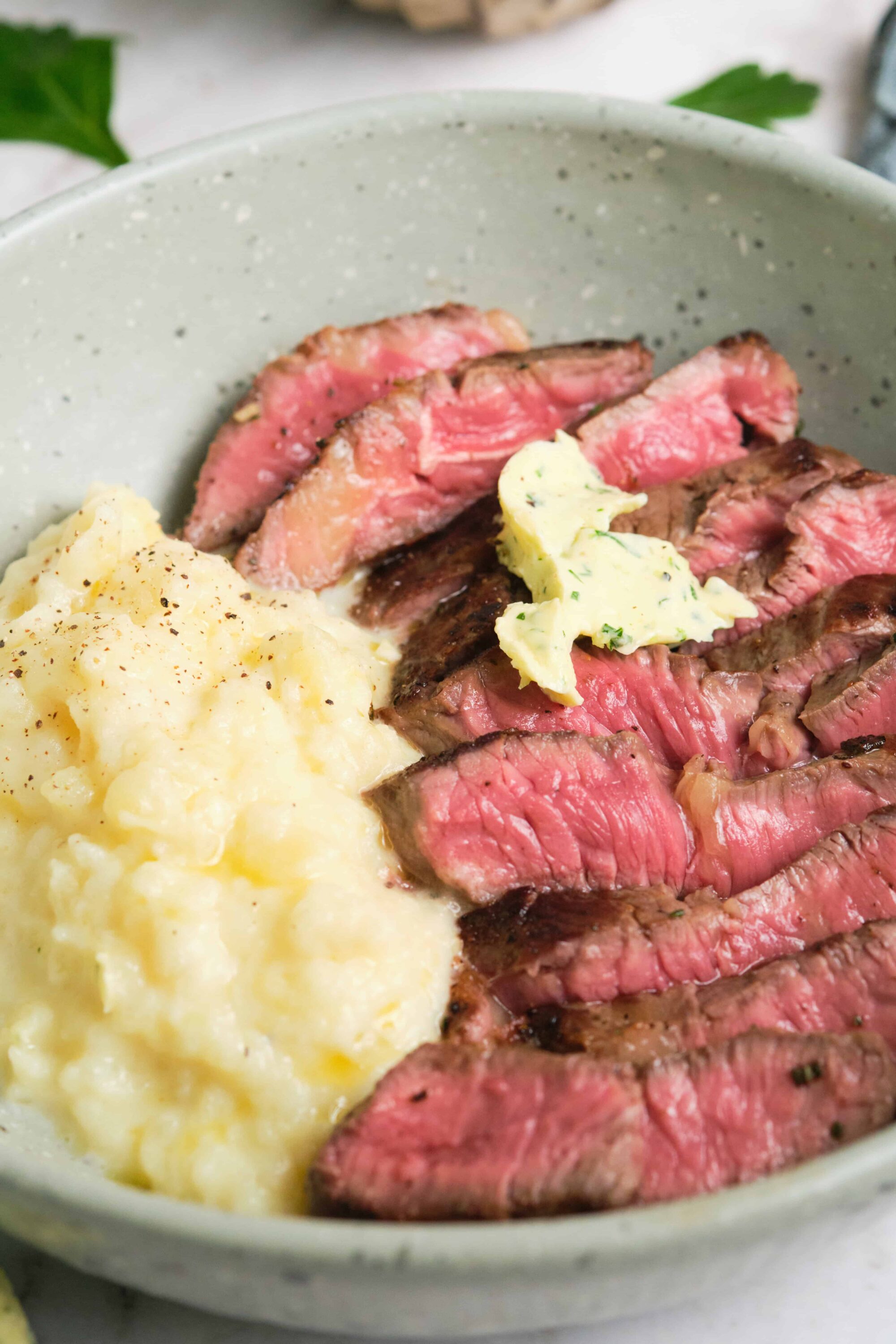 Succulent grilled steak with mashed potatoes and herb butter in a white bowl.