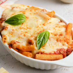 Creamy baked pasta with melted cheese and fresh basil in a white casserole dish.