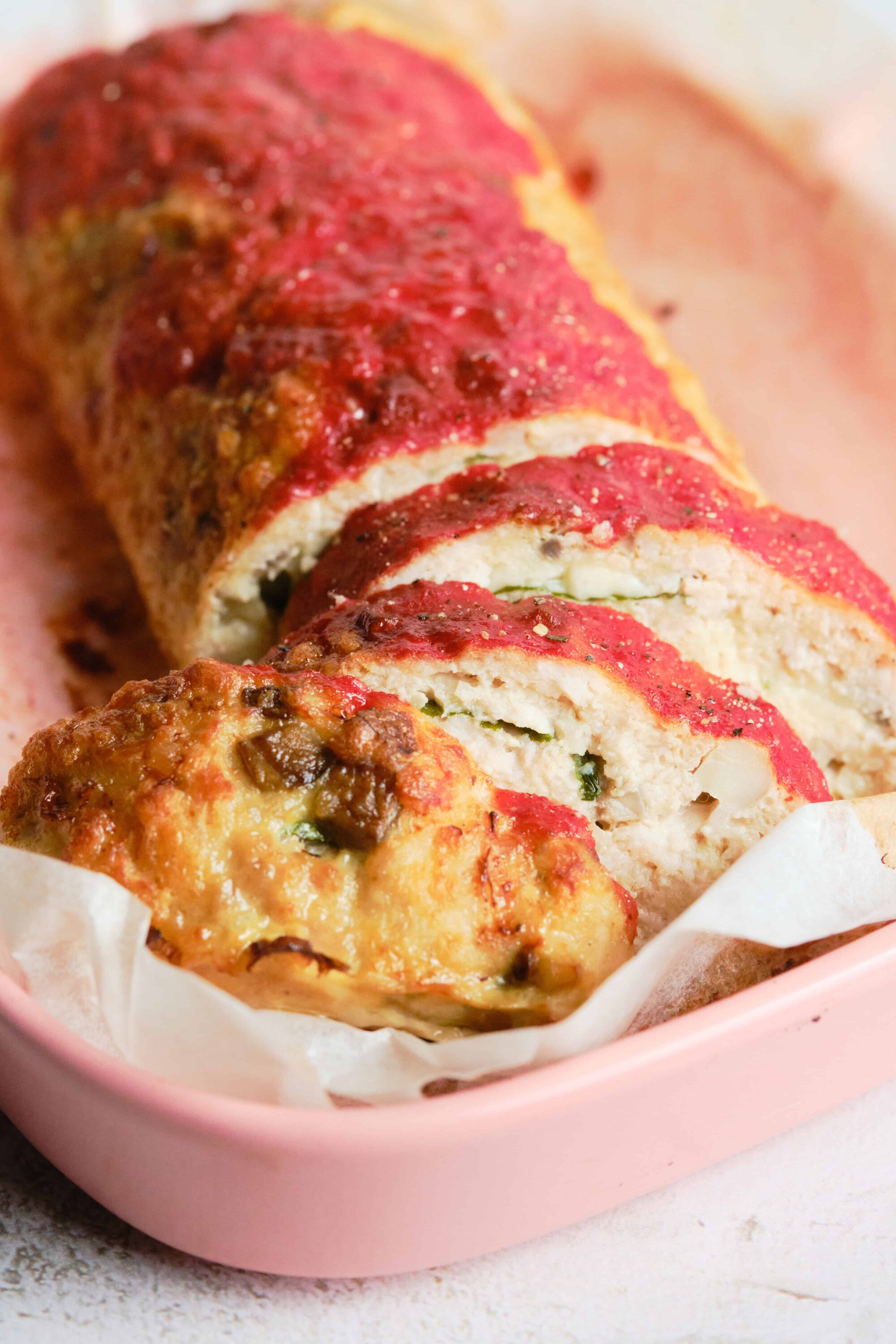 Baked cheese and spinach stuffed chicken breast with marinara sauce in a pink baking dish.
