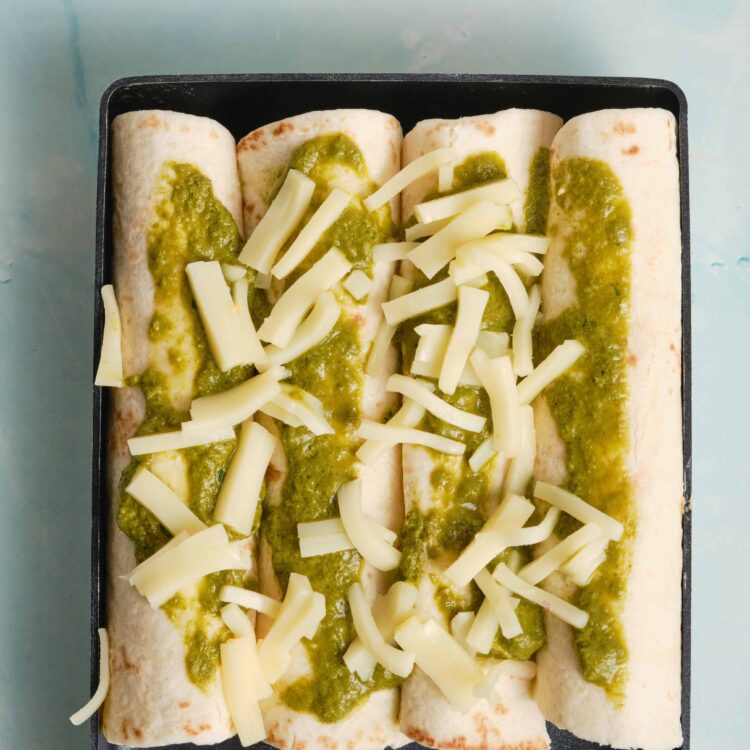 Delicious cheesy baked enchiladas with green sauce and shredded cheese on top.