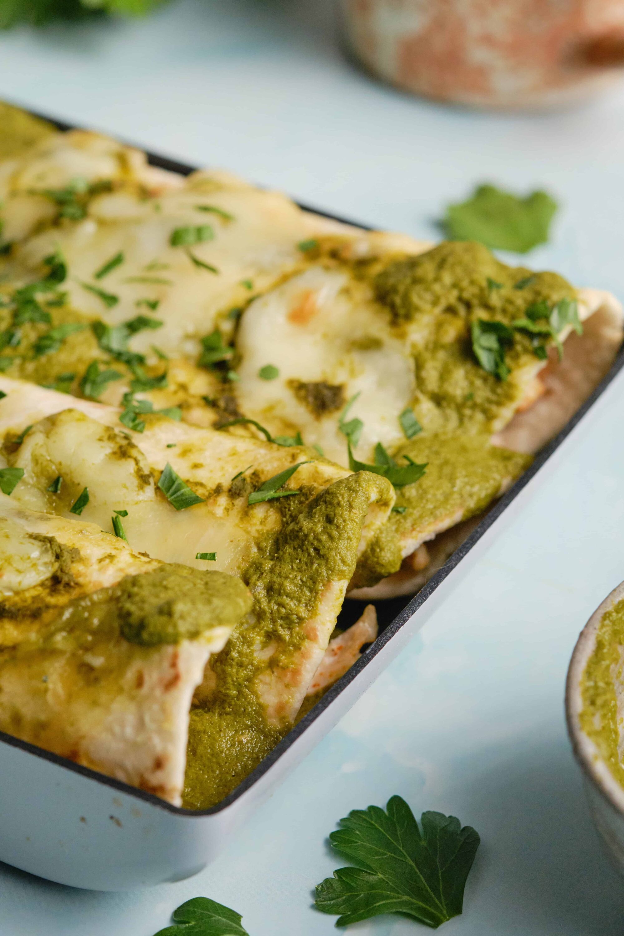 Crispy chicken enchiladas with green sauce and melted cheese in baking dish.