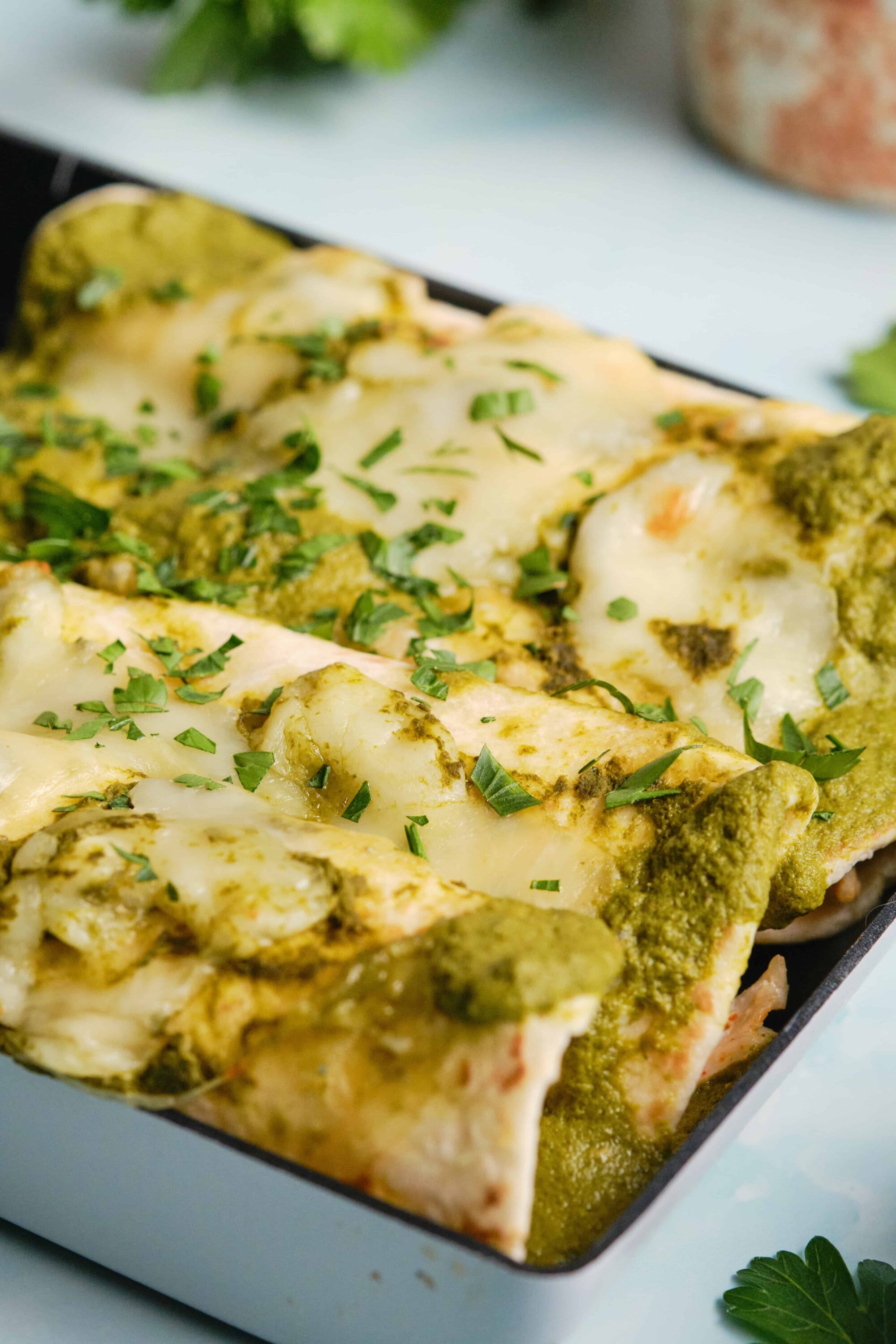 Creamy baked chicken topped with melted cheese and fresh herbs, served with green sauce.