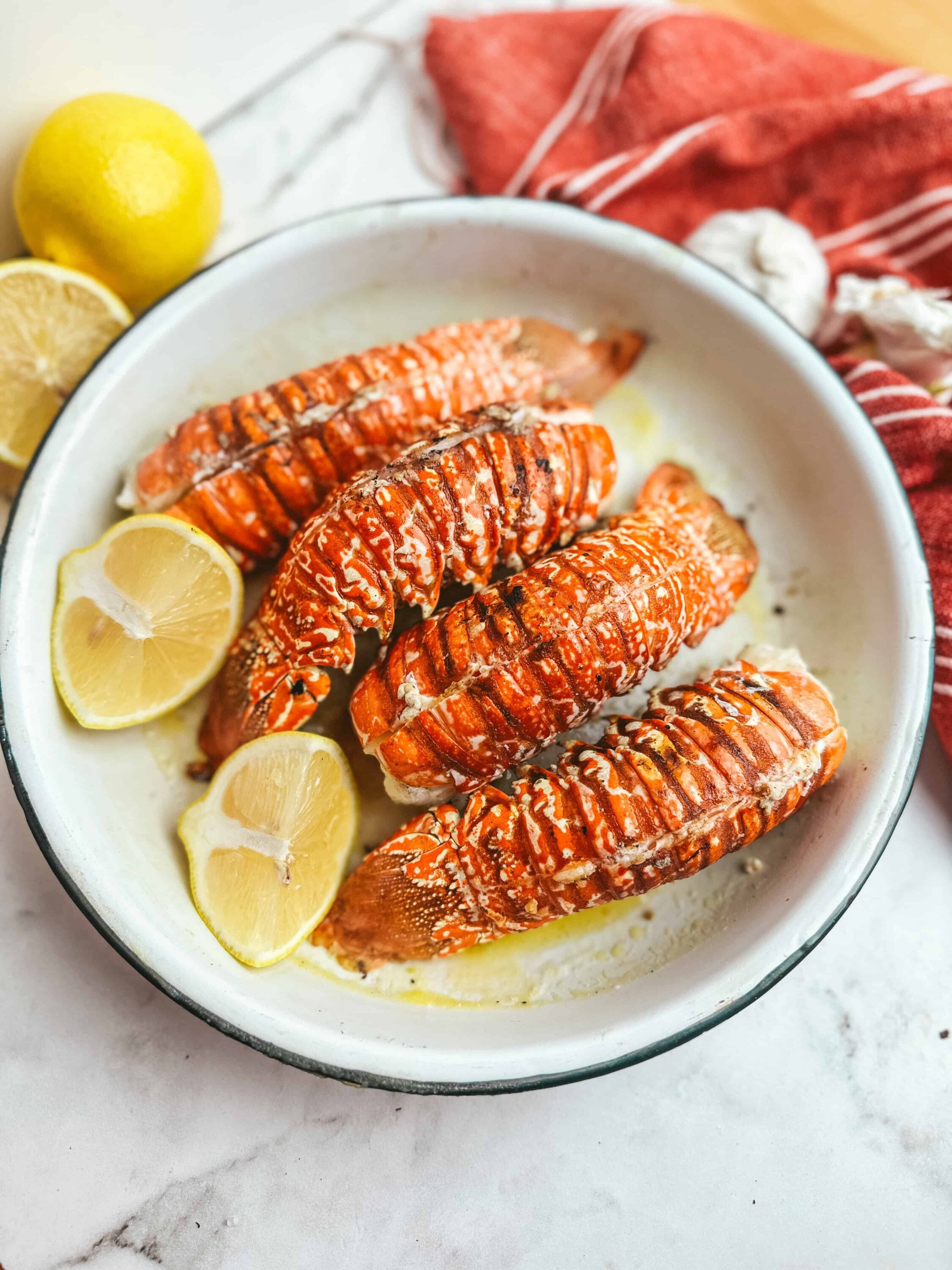 Succulent grilled lobster tails with lemon slices in a white baking dish. Perfect for seafood dinners and special occasions.
