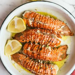 Lobster tails with lemon wedges on a white plate, seafood recipe, baked lobster dish, fresh seafood presentation, Baked Bree recipes.