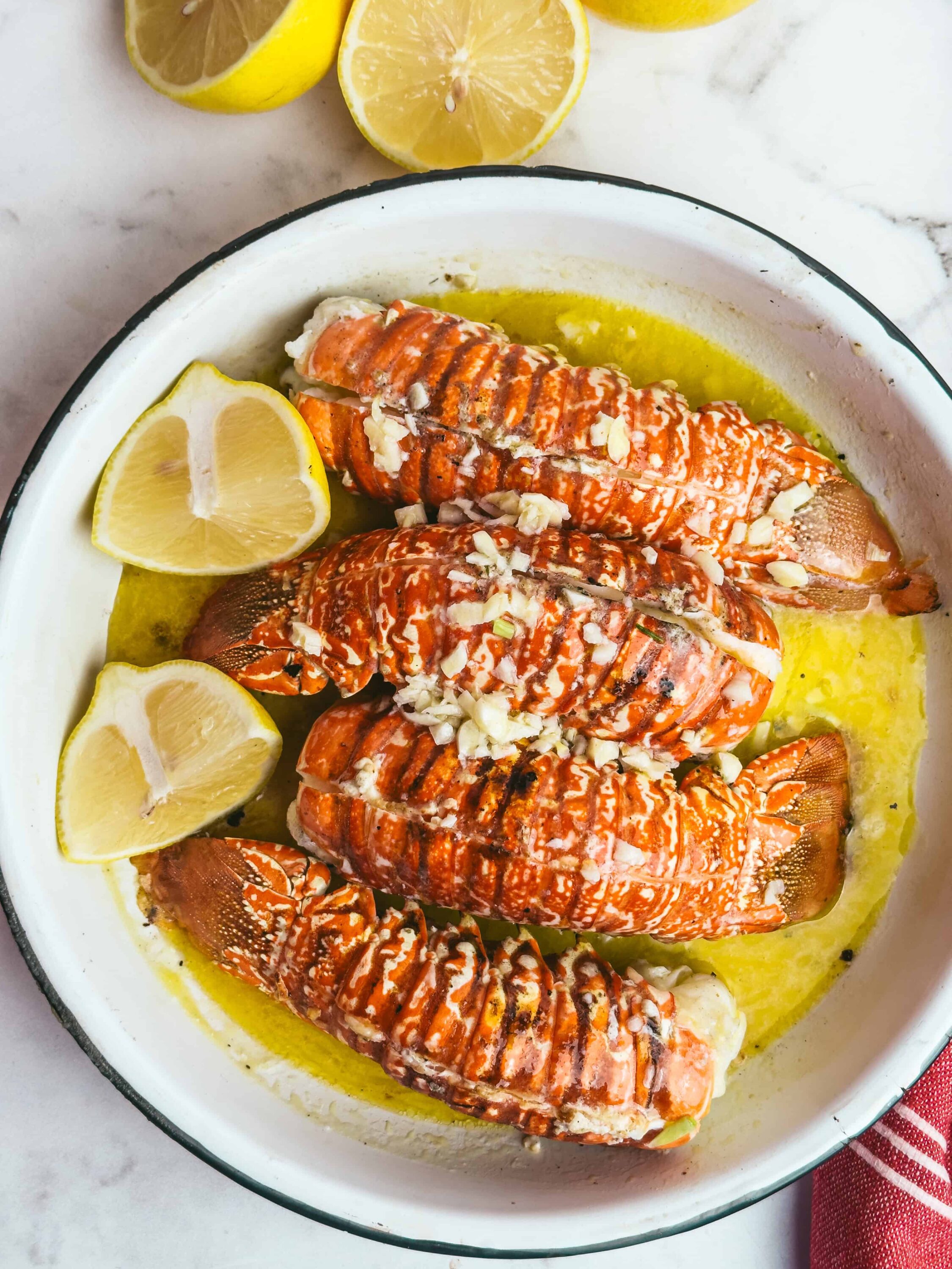 Succulent lobster tails baked with lemon slices and garlic, drizzled with butter, ready for a gourmet seafood feast.