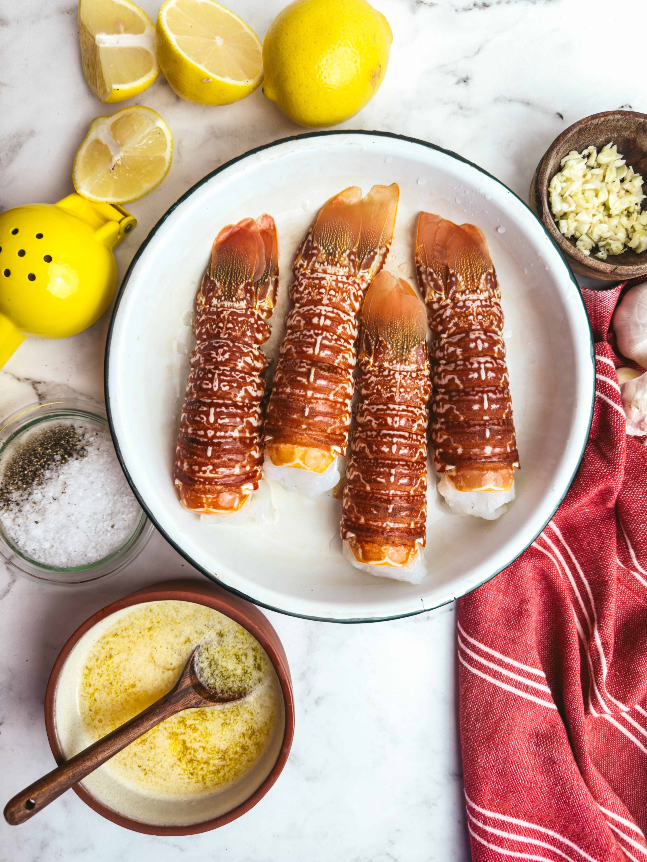 Fresh lobster tails prepared for cooking on a white marble countertop.