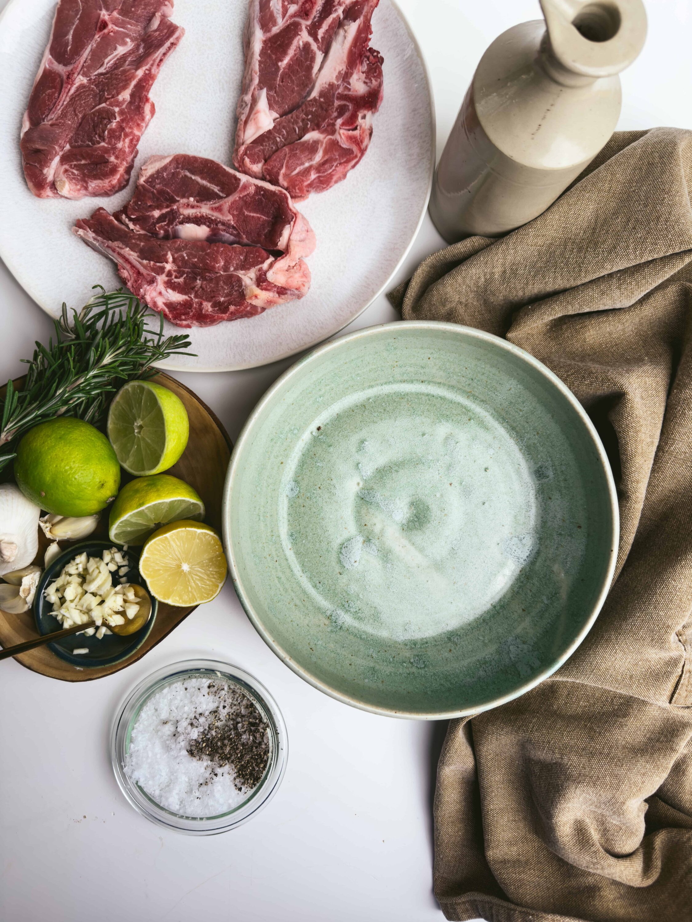 Juicy raw steaks, garlic, herbs, lemons, and seasoning on a kitchen countertop for cooking recipes.