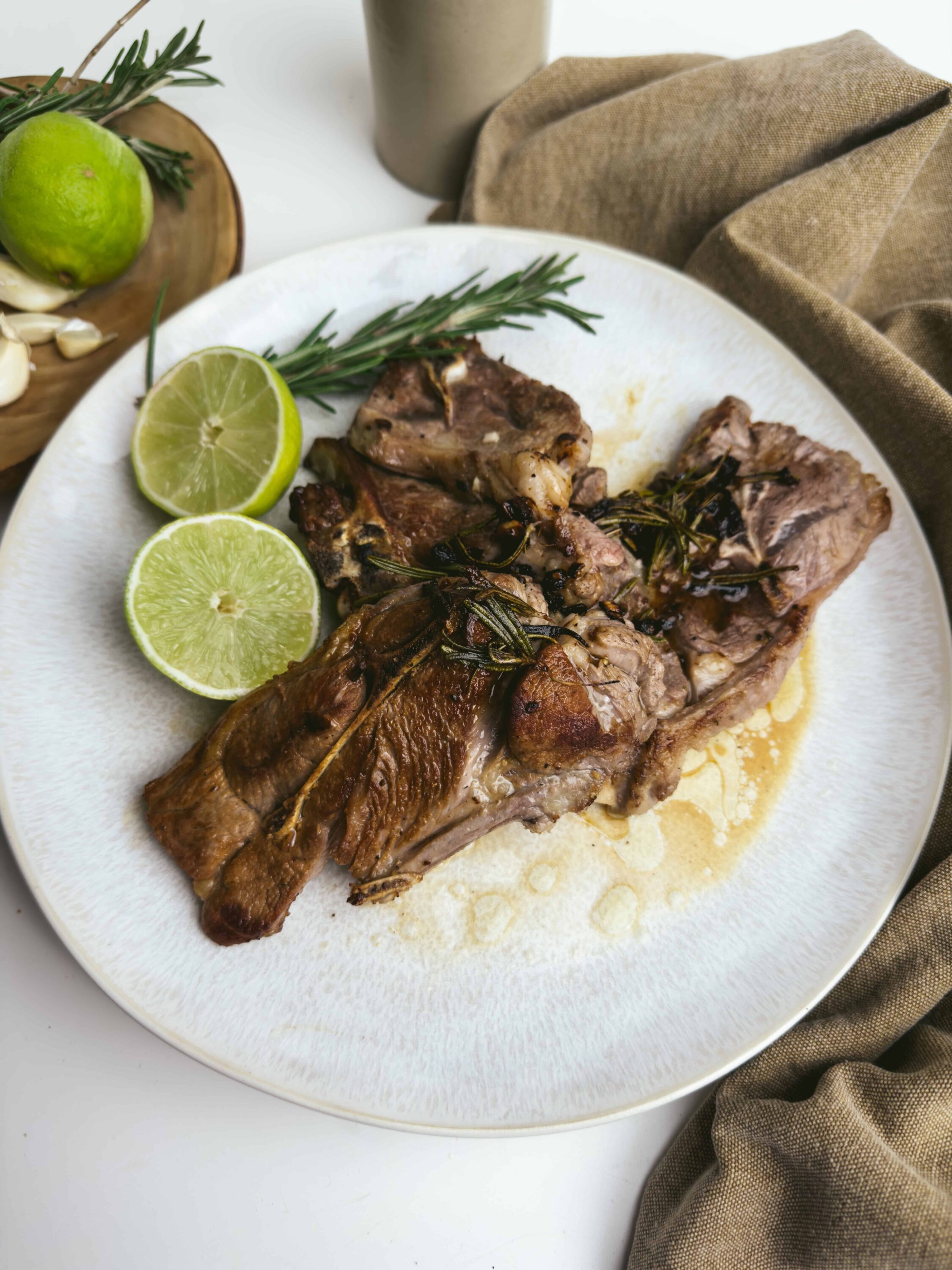 Juicy grilled lamb chops garnished with rosemary and served with fresh lime slices on a white plate.