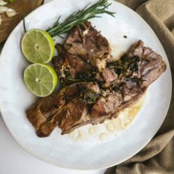 Succulent grilled lamb chops garnished with rosemary and lemon slices, served on a white plate for a flavorful meal.