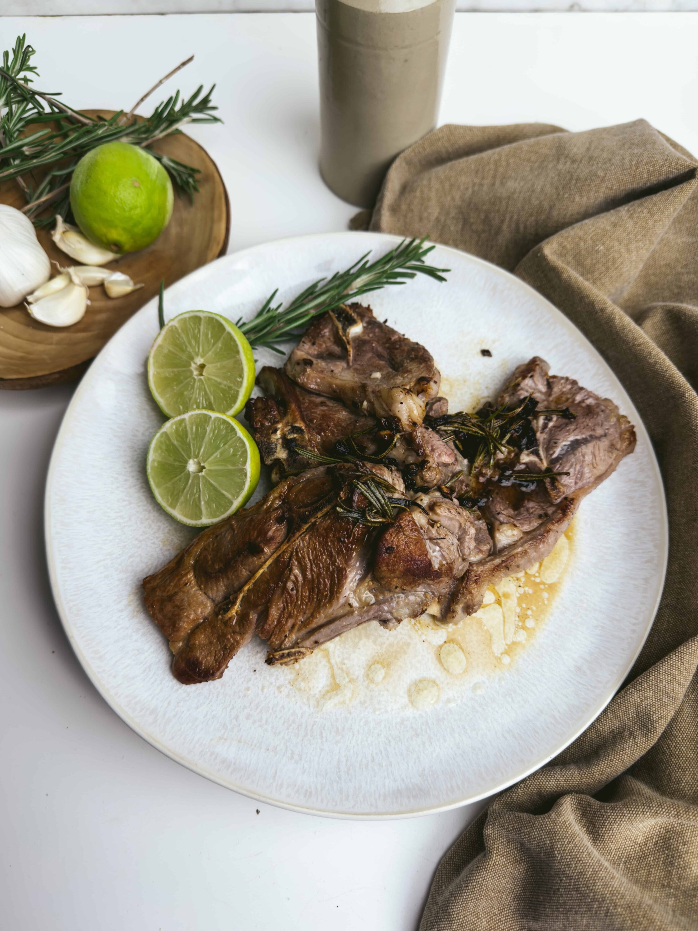 Succulent roasted lamb chops with herbs and lemon slices on white plate.