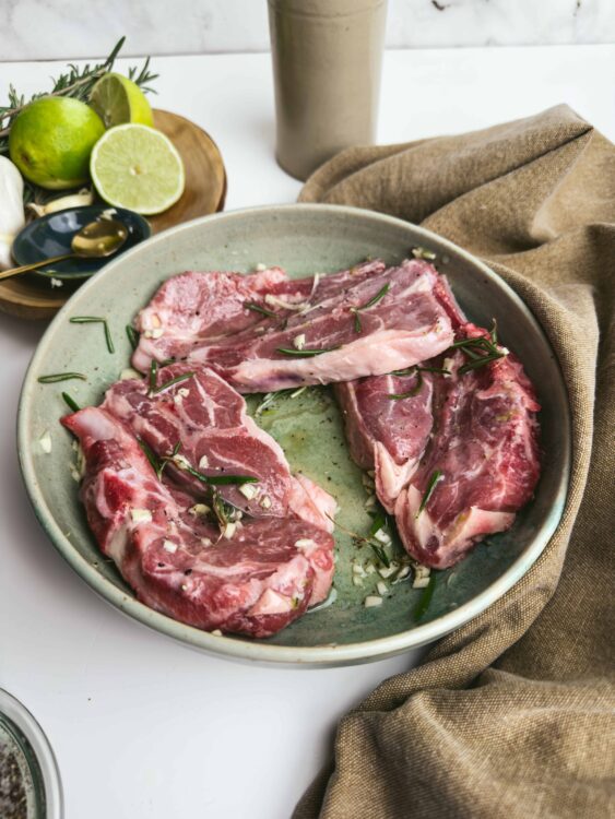 Raw lamb chops seasoned with garlic and fresh herbs on a rustic green plate.