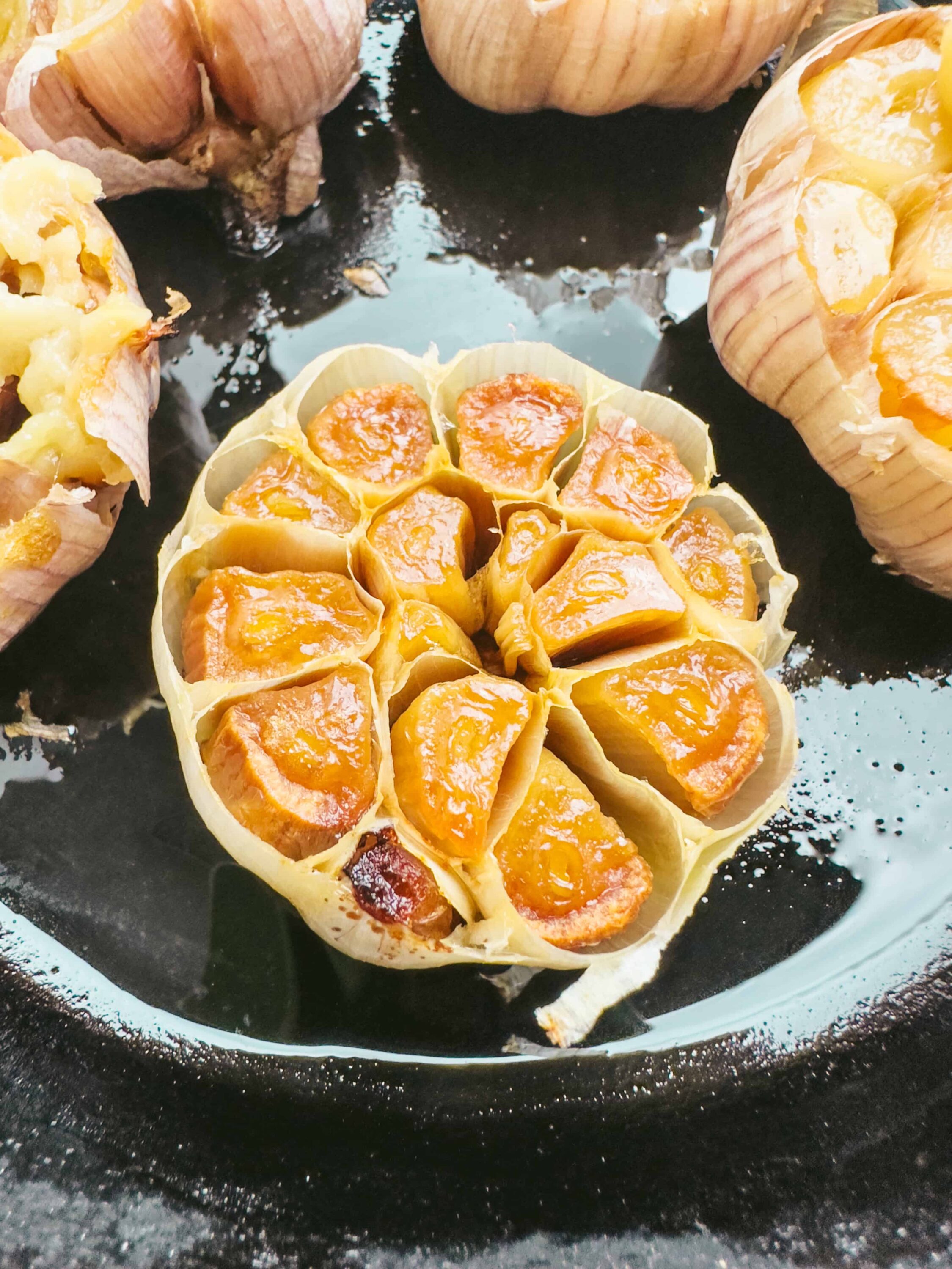 Roasted garlic cloves in parchment paper on black baking sheet.