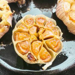 Roasted garlic cloves in parchment paper on black baking sheet.